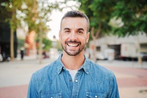 Close up portrait of handsome guy with perfect white teeth smiling and looking at camera standing